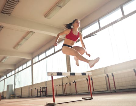 A female athlete demonstrates agility and grace by jumping a hurdle indoors.